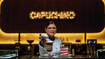 A barista at a coffee bar with a sign reading "CAPPUCCINO" in the background.