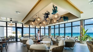 Un espacio interior amplio con mobiliario de mimbre y ventanas grandes que ofrecen vista al océano.