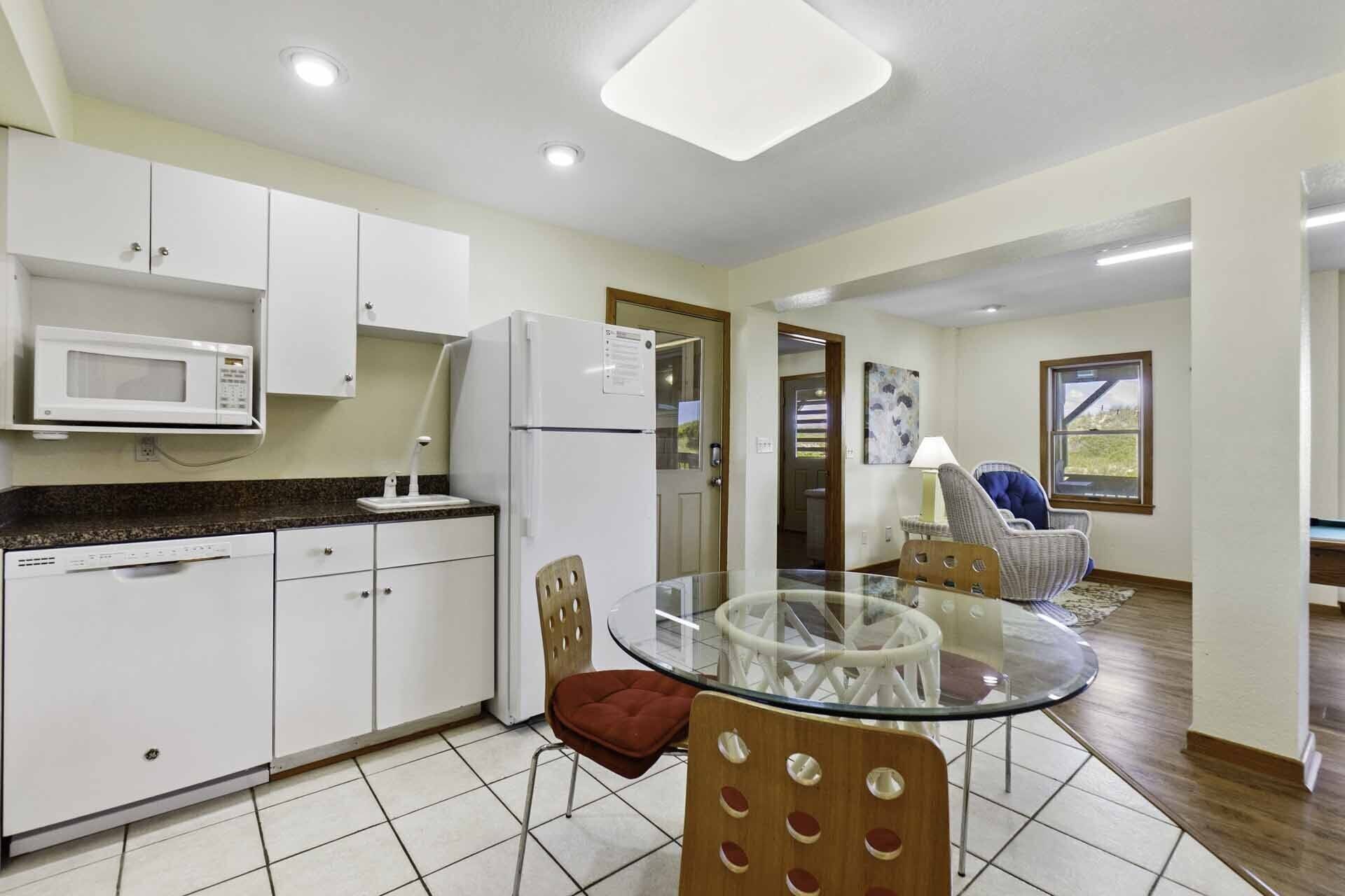 A modern kitchen with white cabinets, a microwave, and a refrigerator. There is a glass table with chairs in the center of the room.