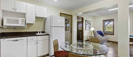 A modern kitchen with white cabinets, a microwave, and a refrigerator. There is a glass table with chairs in the center of the room.