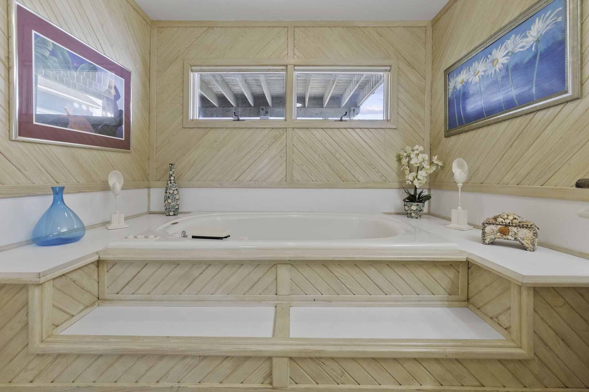 Une salle de bain avec une baignoire sur pieds, deux fenêtres et un lambris en bois.