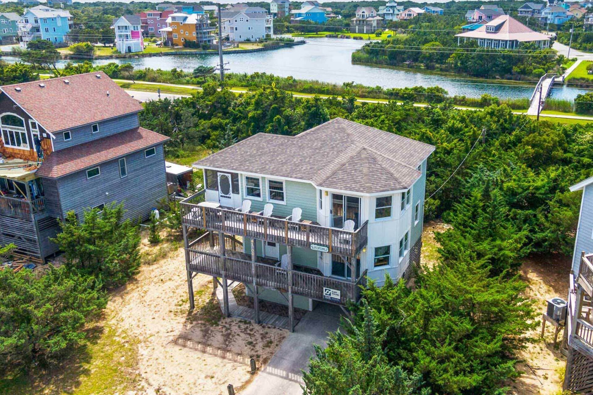 A two-story house with a balcony, surrounded by dense greenery and a lake.