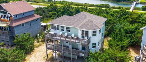 A two-story house with a balcony, surrounded by dense greenery and a lake.