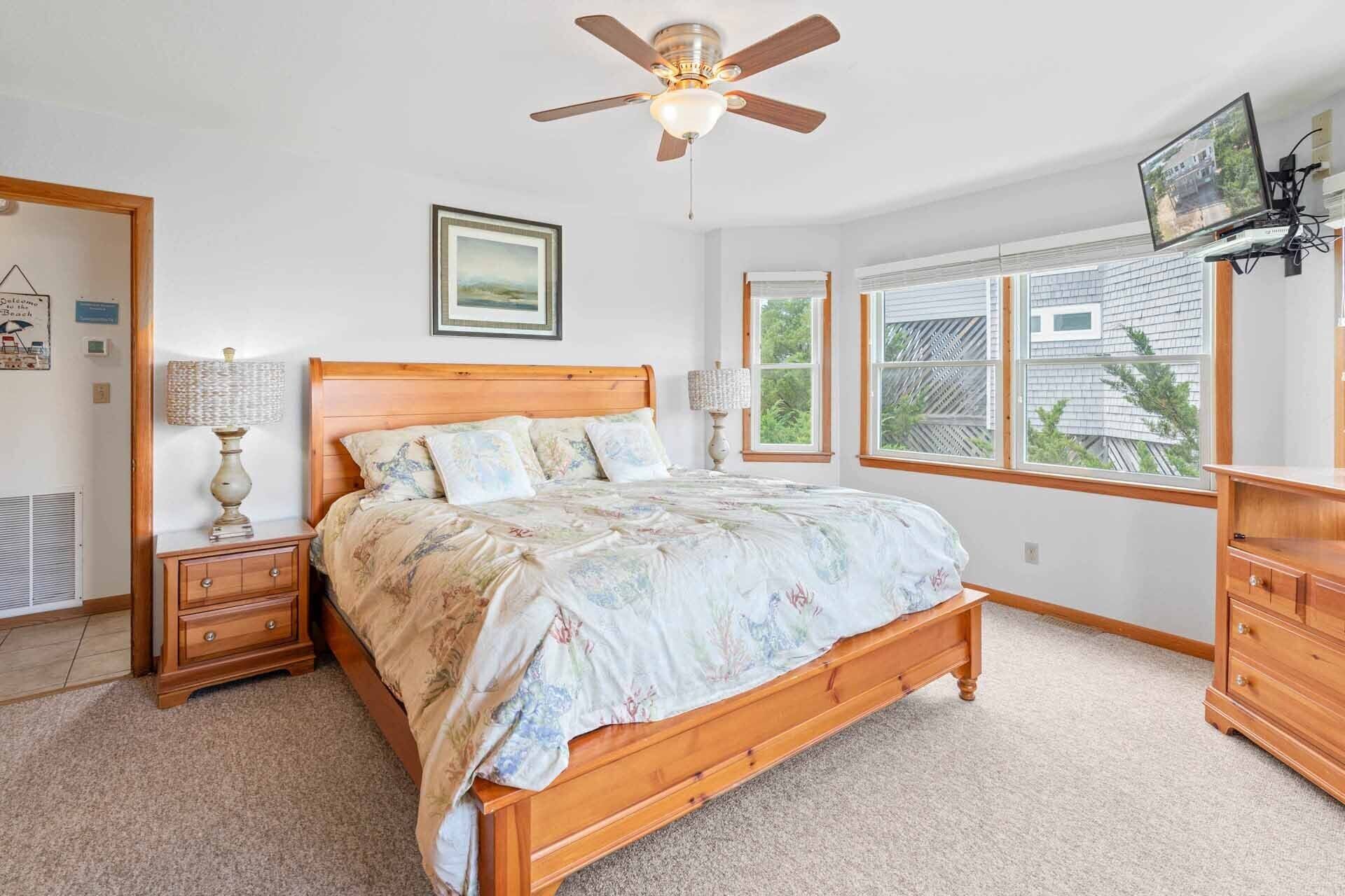 A bedroom with a wooden bed, a ceiling fan, a window with blinds, a dresser, and a framed picture on the wall.