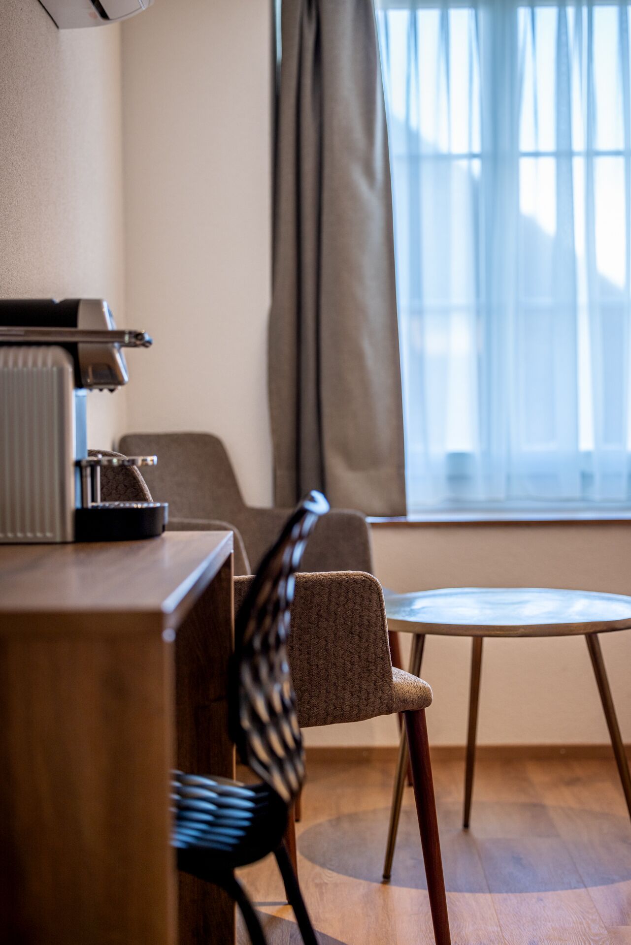 Una habitación de hotel con un escritorio de madera, una silla, una mesita y un ventanal con cortinas.