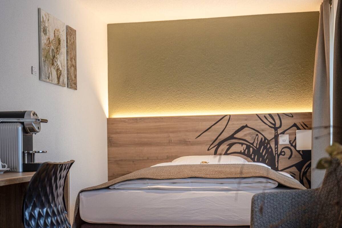 A modern hotel room with a bed, a desk, a chair, and a small table.