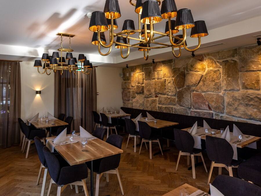 A restaurant with a stone wall, wooden tables, and black chairs.
