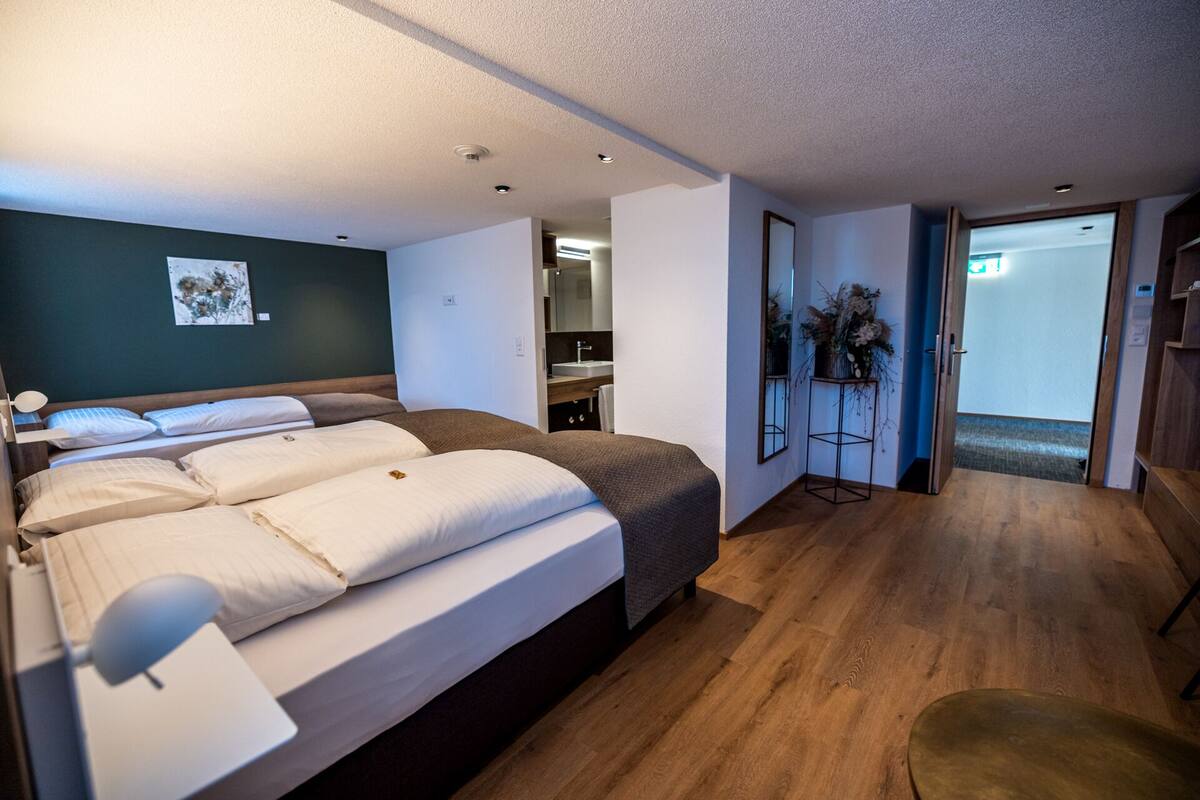 A modern hotel room with a large bed, a bedside table, a mirror, and a small plant.