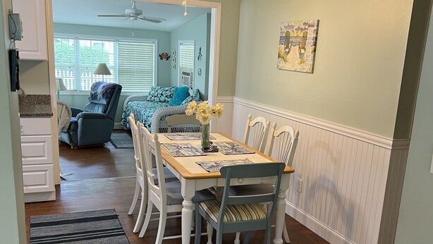A dining area with a wooden table, white chairs, and a ceiling fan.