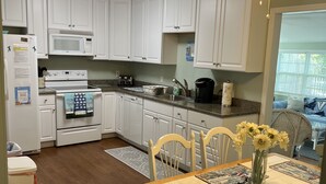 A kitchen with white cabinets, a microwave, stove, and a dining area with a table set for two.