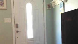 A room with a white door, a flat-screen TV on a white cabinet, and a small rug on the wooden floor.