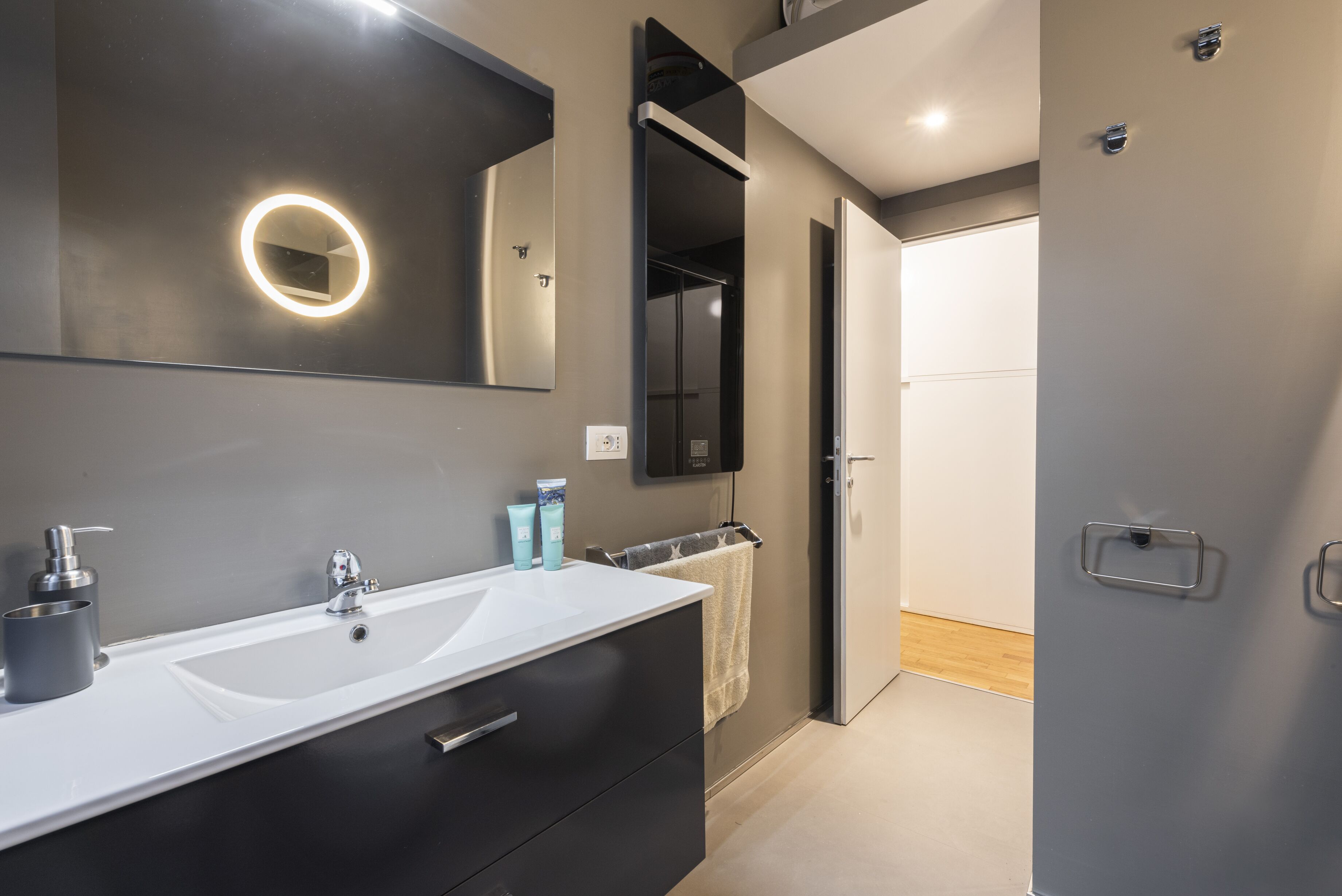 Une salle de bain moderne avec un grand miroir, un lavabo blanc et un porte-serviettes.