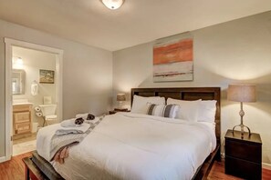 Een net opgemaakt bed met witte lakens, een houten hoofdbord en een bedlampje.