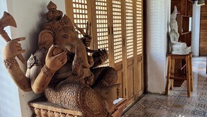 Une statue en bois représentant une divinité à plusieurs bras, placée sur un banc en bois dans une pièce dont le sol est recouvert de carreaux décoratifs et qui possède des portes en bois ornées de motifs en treillis.
