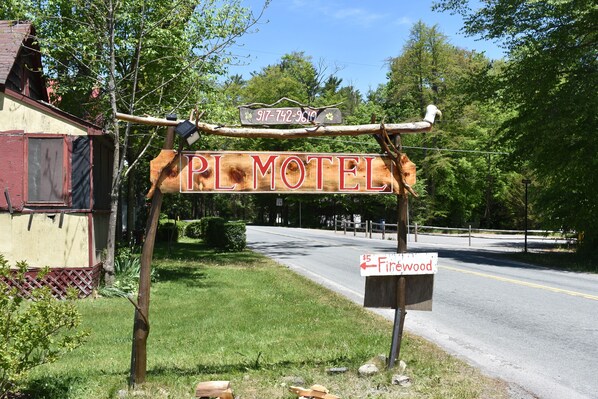 A rustic motel sign with a contact number and a directional sign for Firewood.