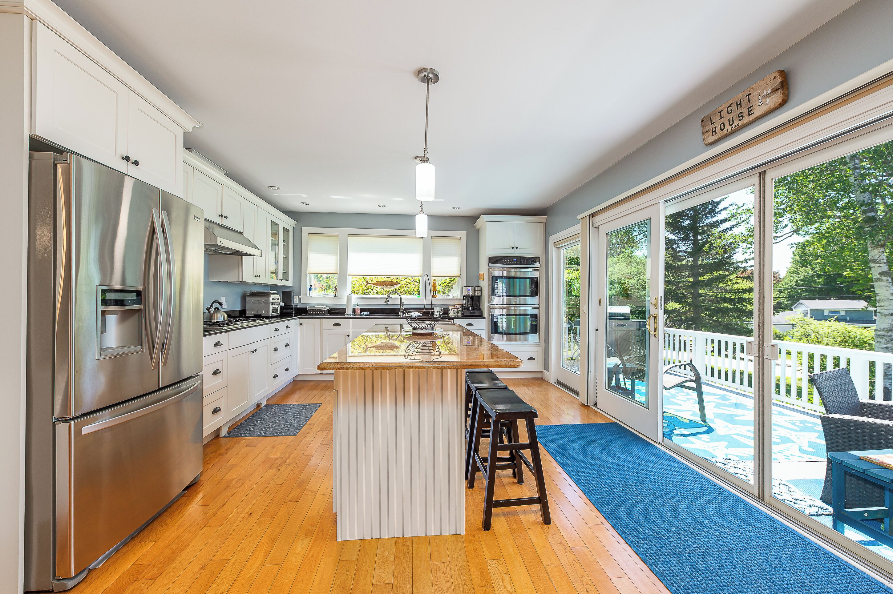 A modern kitchen with stainless steel appliances, a central island with stools, and large windows overlooking a deck.