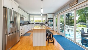 Una cocina moderna con electrodomésticos de acero inoxidable, una isla central con taburetes y grandes ventanas con vistas a una terraza.