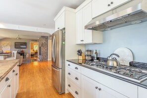 Eine moderne Küche mit weißen Schränken, einem Edelstahlkühlschrank, einem Gasherd und einer Arbeitswand aus Stein.