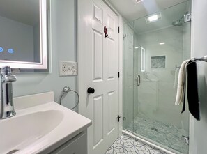 Une salle de bain avec une douche à parois de verre, un lavabo blanc et un miroir au-dessus du lavabo.