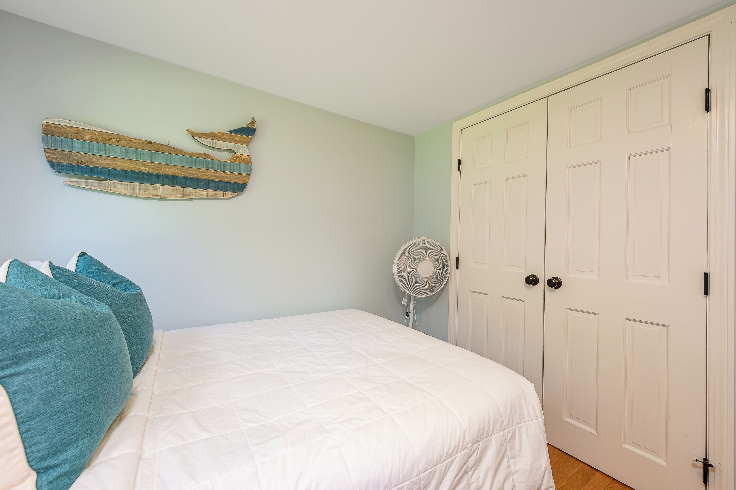 A bedroom with a bed, a wall-mounted fan, and a set of white doors.