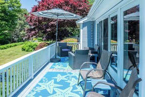 A covered outdoor seating area with wicker furniture, a star-patterned floor, and a large umbrella. - Sand Dollar - Dog-friendly, Steps to the Ocean, Stunning Sunsets (Harpswell)