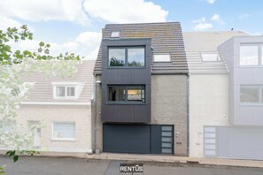 A modern two-story house with a garage, a small balcony, and a window with a view.