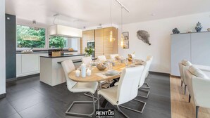 Une cuisine moderne dotée d’un îlot central, de meubles blancs et d’un coin repas avec une table ronde et des chaises.