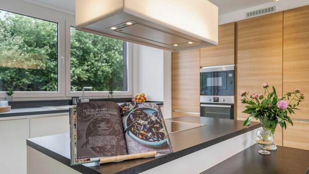 Une cuisine moderne dotée d’une grande fenêtre, d’un four encastré et d’un livre de recettes posé sur le plan de travail.