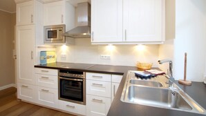 A modern kitchen with white cabinetry, stainless steel appliances, and a black countertop. - Comfort vacation apartment in Wyk, 4 persons, ground floor in 2-family house, 3 rooms, approx. 84m² (Wyk auf Föhr)