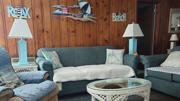 Ein Zimmer mit Holzwandverkleidung, einem blauen Sofa, einem beigen Sessel, einem Glastisch und zwei Lampen.