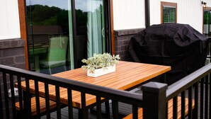 Een houten tafel met een bloempot, een barbecuegrill en een glazen deur naar een terras.