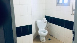 Ein kleines Badezimmer mit Fliesen, einer weißen Toilette, einem Fenster und einer Tür.