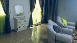 Ein Zimmer mit weißem Schminktisch, einem Spiegel, einem grauen Sofa mit Kissen und einem Fenster mit Vorhängen.