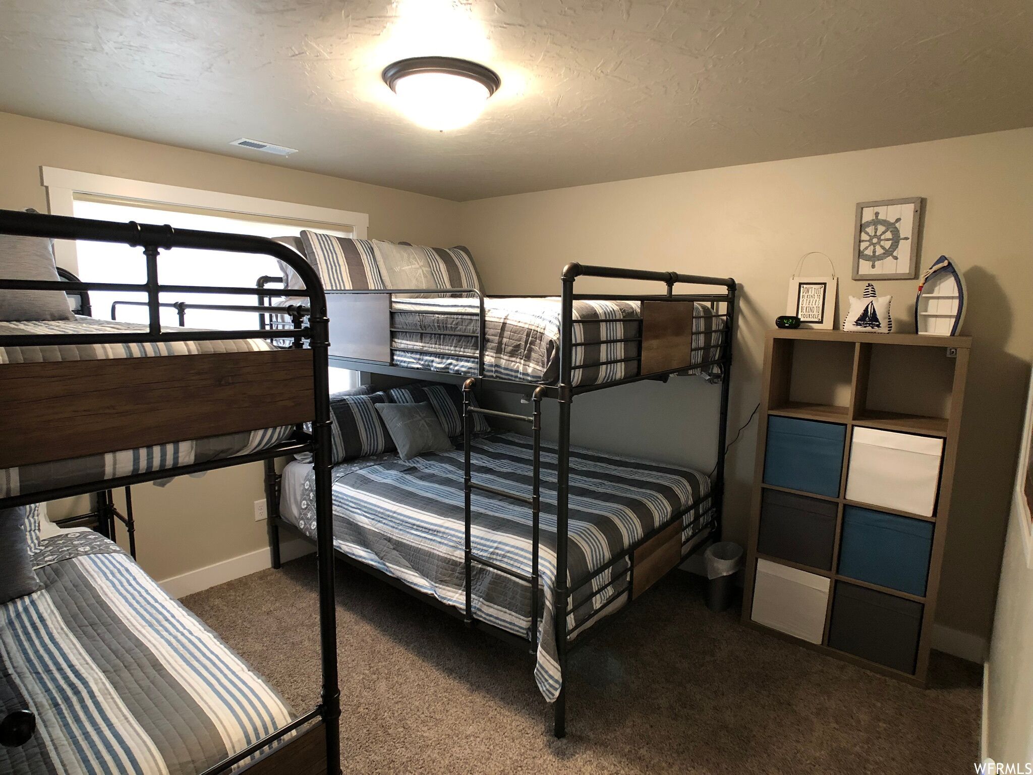 Une chambre avec un lit superposé, une fenêtre, un bureau et une étagère décorative.