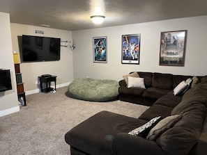 A living room with a brown couch, a green bean bag, a flat-screen TV, and posters on the wall. - Loving Life @ the Lake at Harbor Village! 8 bdrm sleeps 30! Firepit Ping Pong! (Garden City)