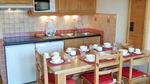 A compact kitchen with wooden cabinets, a microwave, a sink, and a dining area with a table set for four. - 100m from ski slopes, 5th floor, view mountain, balcony, parking, tv, ski locker, 40m², Les 2 Alpes (Les Deux Alpes)