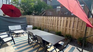 An outdoor patio with a table and chairs, a red umbrella, and a wooden fence. - All new beach block Bartram Beach Tower - 8bd home (Atlantic City)