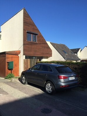Stylish two-story home with a unique architectural style, featuring a brown roof and a driveway with a vehicle.