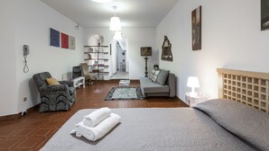 Un dormitorio bien iluminado con cama, sofá, silla y una mesita. Se ve una escalera que conduce a un piso superior.