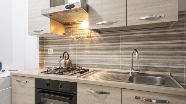 Una cocina moderna con estufa a gas, horno, pileta de acero inoxidable y alacenas de madera.