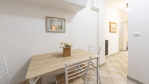 Un comedor con una mesa de madera, sillas blancas y un florero con flores. Hay cuadros en la pared.
