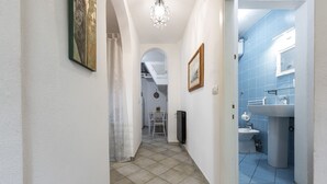 Un pasillo que conduce a un baño con azulejos azules, un lavabo y un cuadro en la pared.