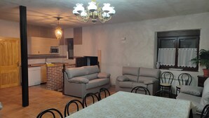 Una sala de estar con una mesa de comedor, dos sofás, una araña y una cocina al fondo.