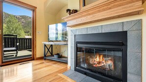 Ein Wohnzimmer mit Kamin, Holzboden und Blick auf einen Balkon mit einer Sitzbank.