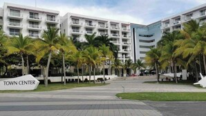 Un hôtel moderne à plusieurs étages, agrémenté de palmiers et d’une enseigne indiquant « Centre-ville » et « Playas Blanca ».