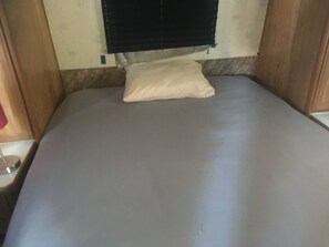 Een kleine kamer met een enkel bed, een grijs matras en een wit kussen.