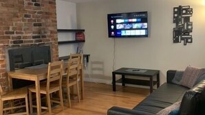 A living room with a fireplace, a TV mounted on the wall, a black leather sofa, and a wooden dining table with chairs. - Cozy 1-bedroom in Bauer Terrace next to Citadel (Halifax)