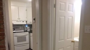 A narrow hallway leading to a kitchen with white cabinets and a stove. - Cozy 1-bedroom in Bauer Terrace next to Citadel (Halifax)