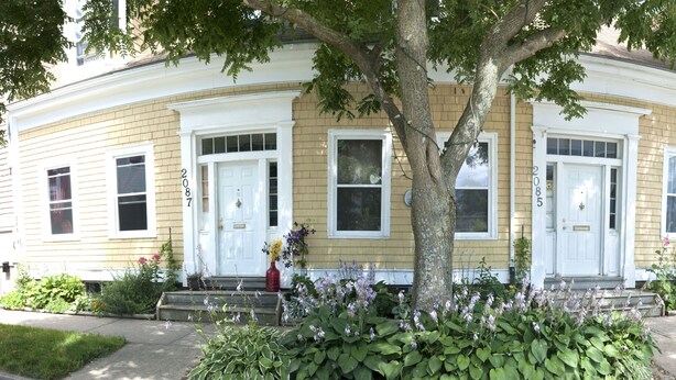 A two-story house with a front porch, a tree in front, and a fire hydrant on the sidewalk. - Cozy 1-bedroom in Bauer Terrace next to Citadel (Halifax)