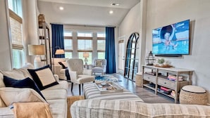 A spacious living room with a large TV, comfortable seating, and a view through a glass door.